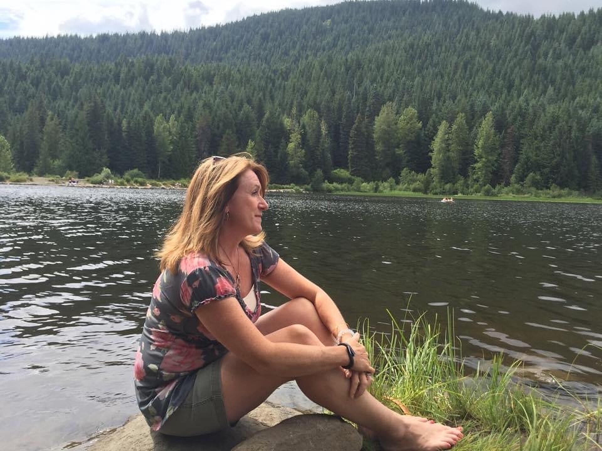 Carolyn Lorente seated beside a lake with forested hills in the background.
